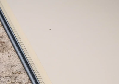 Joint en métal gris séparant un sol en pierre beige d'une surface blanche lisse.