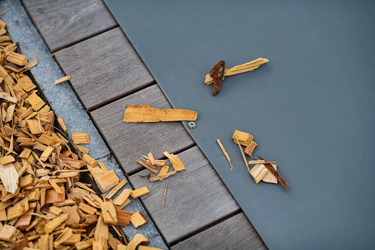 Des éclats de bois sont dispersés sur une couverture de piscine grise, à côté de dalles en bois.