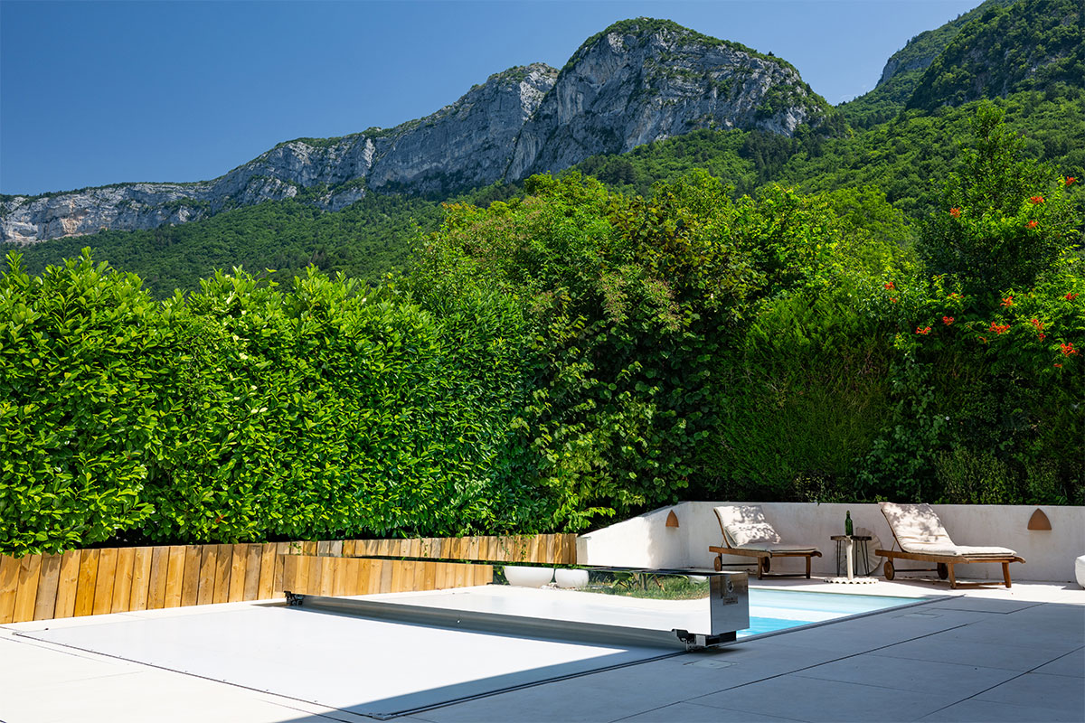 Piscine équipée d’une Coverseal, entourée de haies hautes et d’un paysage montagneux en arrière-plan, avec transats installés près de l’eau.
